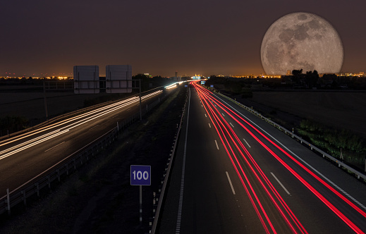 Night road with the city in the background and a spectacular moon. Wakes of the cars