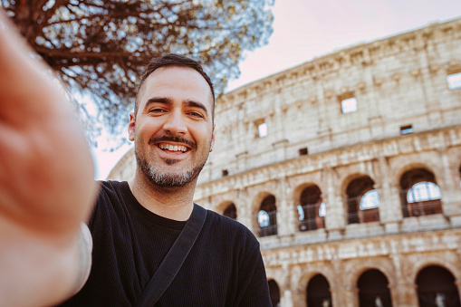 Young happy smiling caucasian man taking selfie, in front of Colosseum, Rome, Italy. Holiday, travel, vacation, tourist, summer concept.