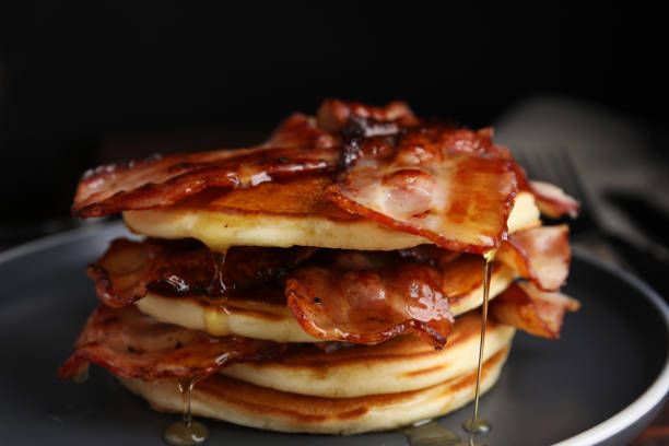 istock Delicious pancakes with maple syrup and fried bacon on plate, closeup 1412855311
