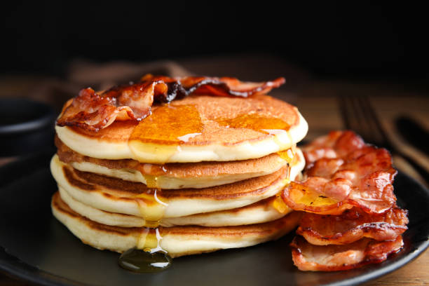istock Delicious pancakes with maple syrup and fried bacon on plate, closeup 1412855350