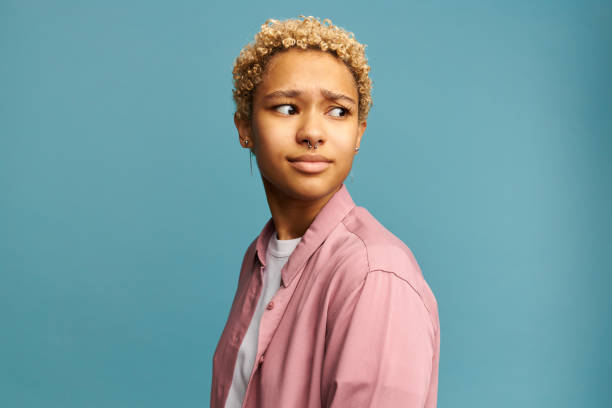 istock Sad pretty girl feeling upset while spending time at home alone. Beautiful young dark-skinned female with Afro hairstyle staring at camera with unhappy or regretful look against studio wall 1412855386