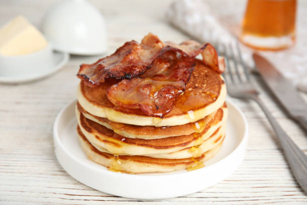istock Delicious pancakes with maple syrup and fried bacon on white wooden table, closeup 1412855409