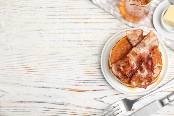 istock Delicious pancakes with maple syrup and fried bacon on white wooden table, flat lay. Space for text 1412855555