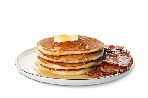 Delicious pancakes with maple syrup, butter and fried bacon on white background