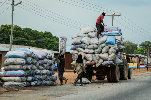 Accra, Ghana - April 06, 2022: African Workers moving the Heavy Bags on Ghana Road