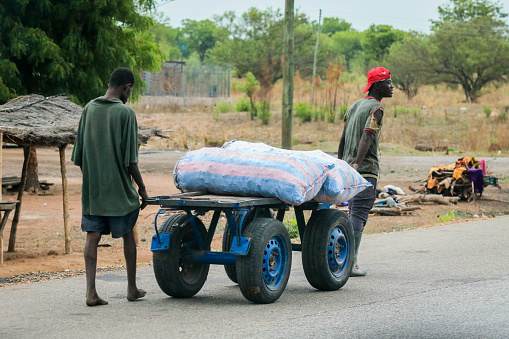 Accra, Ghana - April 06, 2022: African Workers moving the Heavy Bags on Ghana Road