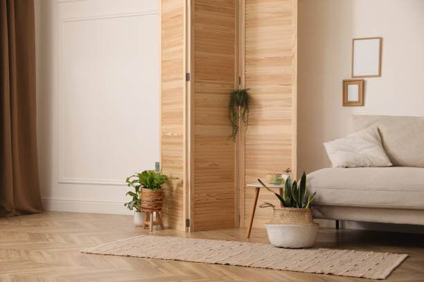 istock Stylish room with wooden folding screen and comfortable sofa near white wall. Interior design 1412857236