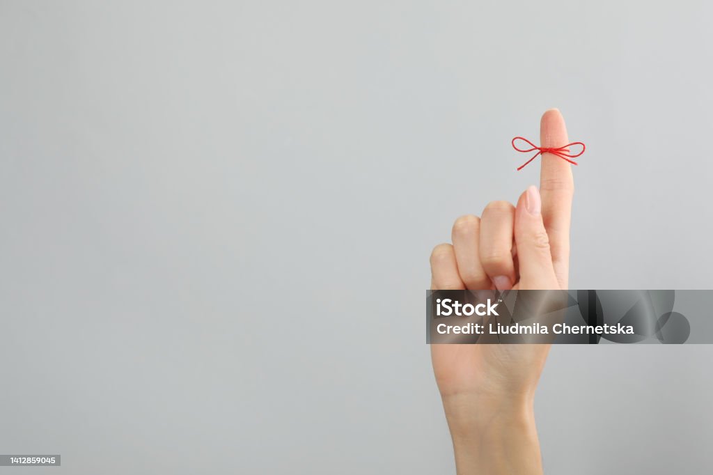 Woman showing index finger with tied red bow as reminder on light grey background, closeup. Space for text Reminder Stock Photo