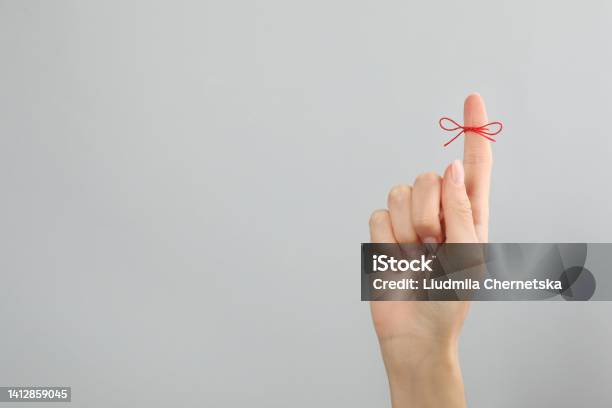 Woman Showing Index Finger With Tied Red Bow As Reminder On Light Grey Background Closeup Space For Text Stock Photo - Download Image Now