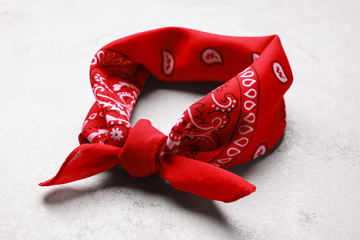 Tied red bandana with paisley pattern on light table, closeup