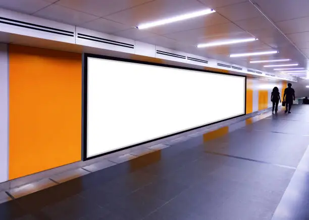 Photo of Long horizontal long mock up of blank advertising billboard poster template in a long tunnel walkway; out-of-home OOH media display advertisement mockup in pedestrian underpass; digital display.