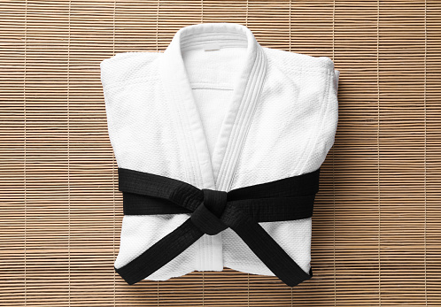 Martial arts uniform with black belt on bamboo mat, top view