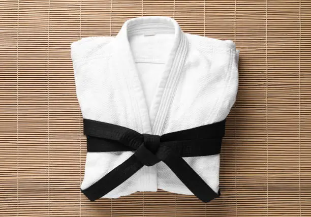 Martial arts uniform with black belt on bamboo mat, top view