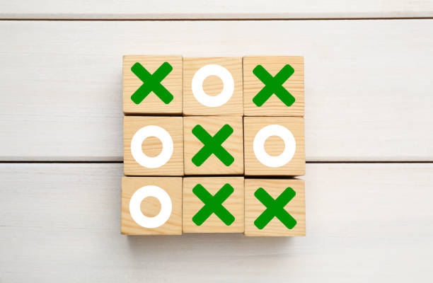Two businesswomen are taking a break from work, enjoying a friendly game of tic-tac-toe, placed on top of a laptop, fostering camaraderie and a relaxed atmosphere