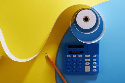 adding machine tape and blue caculator against blue and yellow background