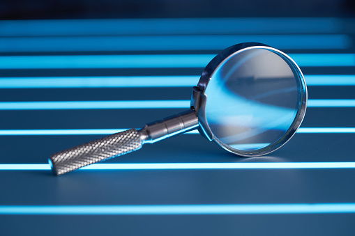 A magnifying glass leans against a thick stack of papers. Photographed with a very shallow depth of field.