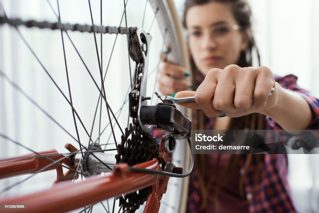 Woman fixing her bicycle at home Confident woman fixing her own bicycle at home, she is using a spanner and checking wheels Bicycle Stock Photo