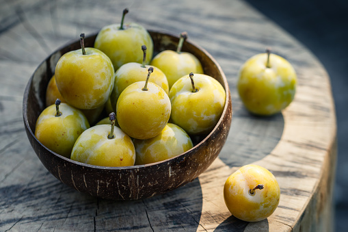 Whole and sliced red plums in a metal bowl on a dark gray background