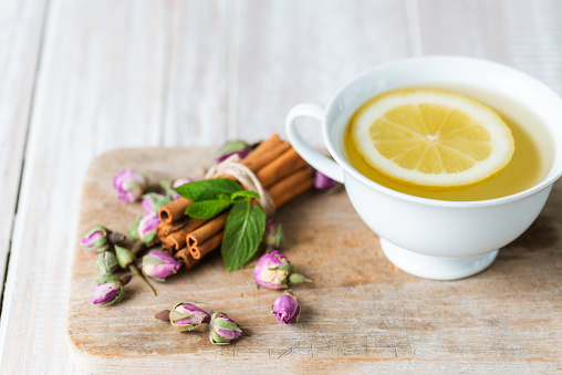 Herbal tea with lemon slice on a white wooden table with dried plants and cinnamon.