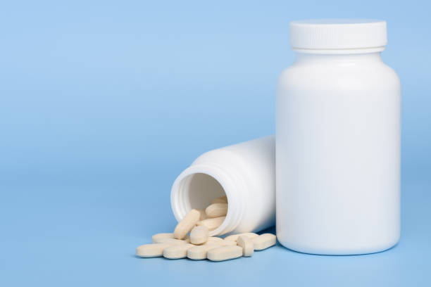 istock Two white medicine bottles, one closed and second with pills spilled on blue background 1412869159