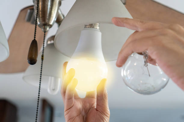 istock Power saving concept. Asia man changing compact-fluorescent (CFL) bulbs with new LED light bulb. 1412869413