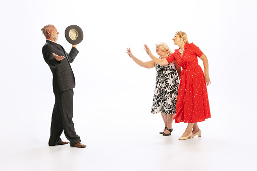 Meeting. Handsome senior man and two charming women in vintage retro style outfits dancing isolated on white background. Concept of relations, family, 1960s american fashion style and art.