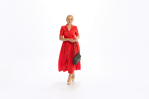 Fashion model. Portrait of beautiful senior woman in retro vintage red dress posing isolated on white background. Concept of beauty, old generation, fashion, emotions. Copy space for ad