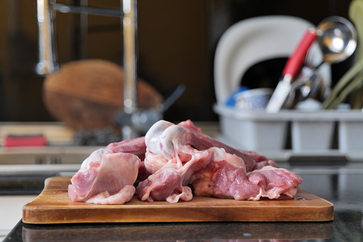 On the picture there are raw turkey bones with some meat on them lying on a wooden chopping board in the kitchen of a home. In the background we see the sink and other things related to dishwashing.