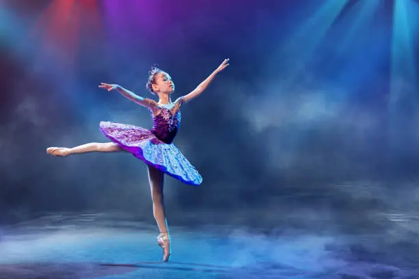 Photo of A little Japanese ballerina dances on stage in a lilac tutu on pointe shoes classical ballet.