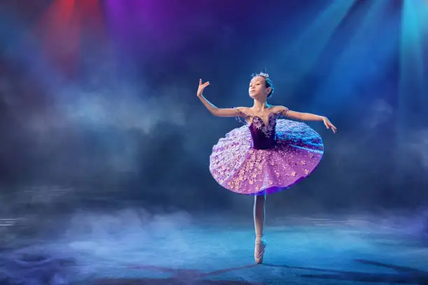 Photo of A little Japanese ballerina dances on stage in a lilac tutu on pointe shoes classical ballet.