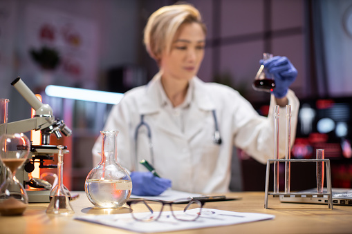 Focus on test tube. Scientific innovations. Positive smart enthusiastic woman scientist looking at the test tubes and smiling while developing a vaccine.