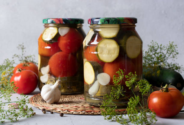 istock Marinated zucchini with tomatoes in two glass jars for the winter on a light background with fresh ingredients 1412878458