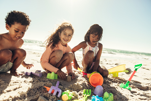 Group of happy kids playing with their toys on beach sand. Three carefree children having a good time at a sunny beach during summer vacation.