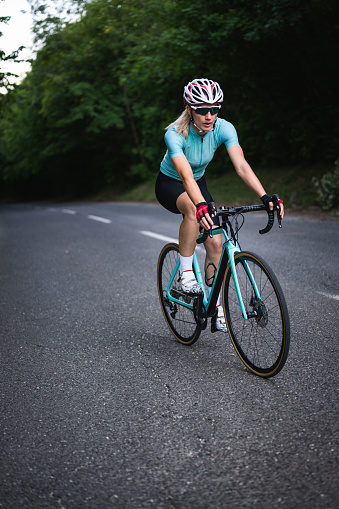 Professional female cyclist trains in the woods. Woman riding race bicycle on a forest asphalt road, uphill, front view