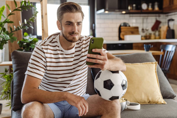 istock Young man with soccer ball, using smart phone 1412882019
