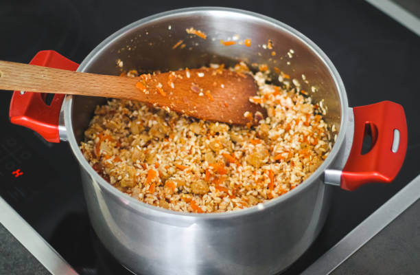 istock Semi-cooked minced meat with rice and vegetables in a saucepan with red handles . 1412882425