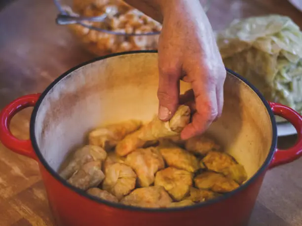 Hands of a seigners woman laying raw sauerkraut stuffed cabbage and rice-meat stuffing in a cast-iron pan while sitting at a round table in the kitchen, close-up top view. The concept of step by step instructions, home cooking, traditional recipes, national cuisine, cabbage rolls, dolma.