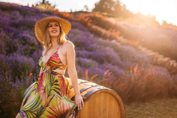 Beautiful young woman in lavender field, leaning on a barrel.