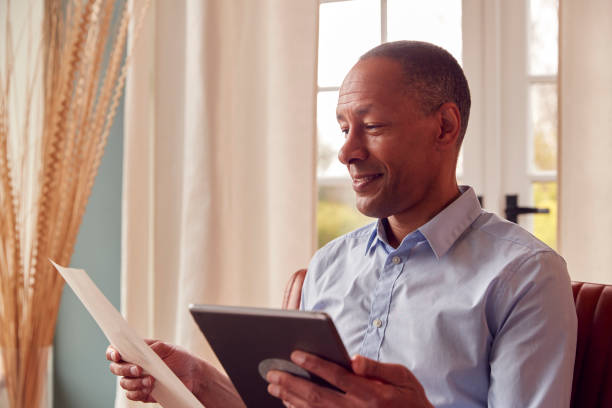 istock Mature Man Or Businessman Working From Home Sits In Armchair Reading Document Using Digital Tablet 1412884198
