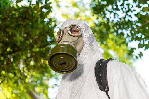 Man spraying insecticide on grass in lawn. Man in mask and protective suit spraying insecticides and parasites in the garden.