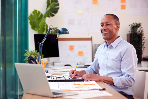 istock Mature Male Architect Working In Office At Desk Studying Plans For New Building 1412887714