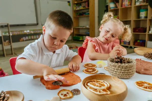 Children making prints on the dough using natural materials dry orange slices, cones, shells, feathers in kindergarten. Early development concept. Selective focus on boy.