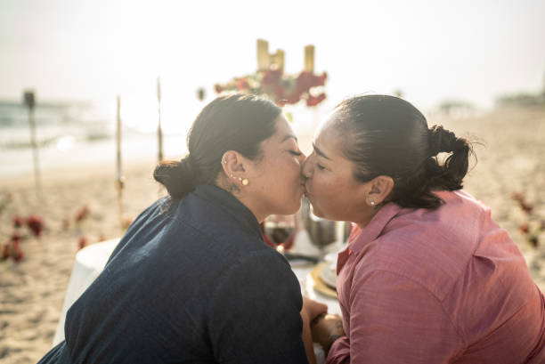 un couple de lesbiennes s’embrasse lors du dîner sur la plage - lesbian homosexual kissing homosexual couple photos et images de collection