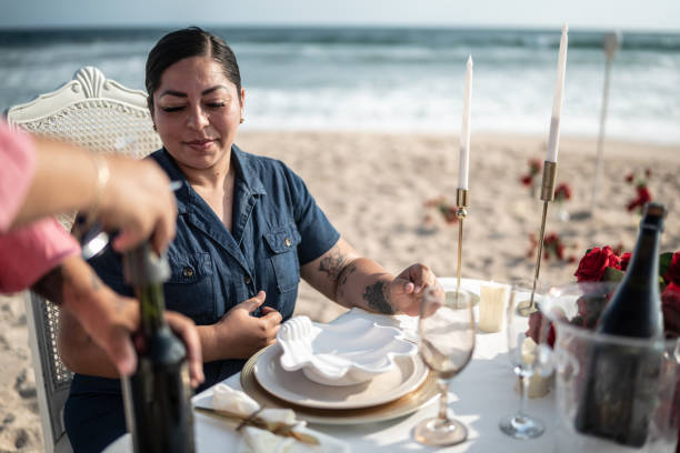 istock Mature woman open a wine bootle for her girlfriend at a dinner on the beach 1412891901