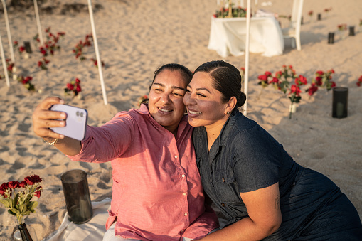 Lesbian couple taking a selfie using mobile phone at the beach