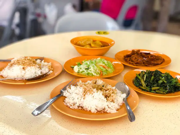 A spread of rice and dishes on a table at coffeeshop. Economy mixed rice with vegetables and meat is popular in Singapore and Malaysia. Selective focus