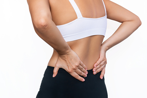 Cropped shot of a young woman holding her lower back with her hands isolated on a white background. Back pain. Sciatica, osteochondrosis, gallstone disease, pancreatitis. Sports injury