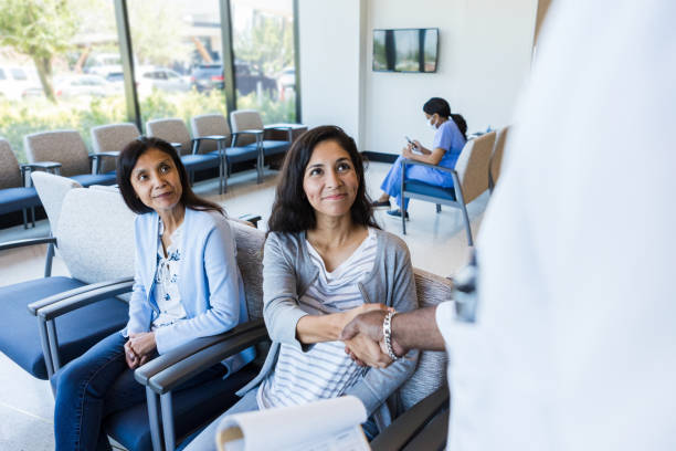 Mother watches as daughter shakes hands with ER doctor Sitting in the emergency room lobby, the mature adult mother watches as her young adult daughter shakes hands with an unrecognizable doctor. emergency medicine stock pictures, royalty-free photos & images