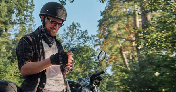 istock Young male biker in helmet using mobile phone and smiling sitting on a motorcycle 1412899169