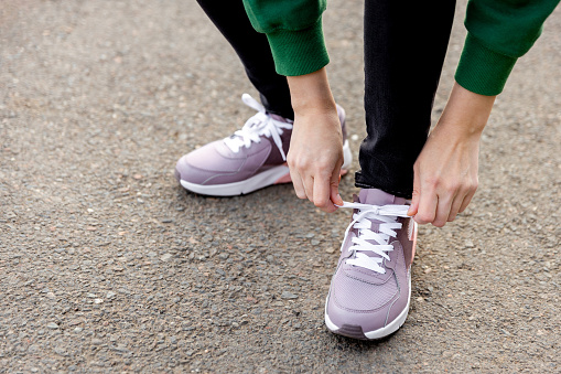 woman stands on an asphalt road and ties her shoelaces. Womans legs in pink sneakers close up